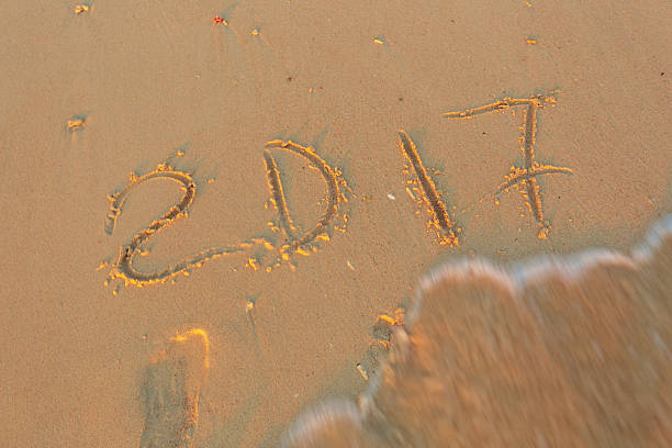 A person writes the numbers 2017 in the sand on a beach at sunset.