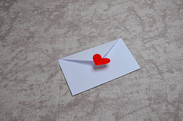 A hand holds an open white envelope with red and pink paper hearts scattered on the table, symbolizing a Valentine’s Day message, love letter, and romantic feelings.