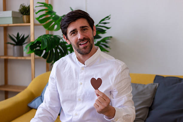 Young adult man smiling, holding a heart cutout celebrating love and affection