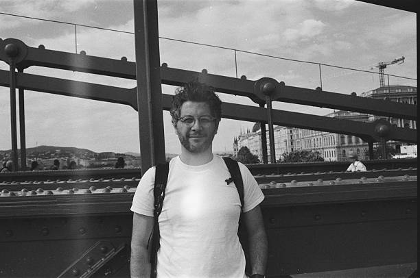 A man is standing on a city bridge in Budapest during a spring weekend trip, photographed in daytime on black and white 35mm analog film with an analog camera.