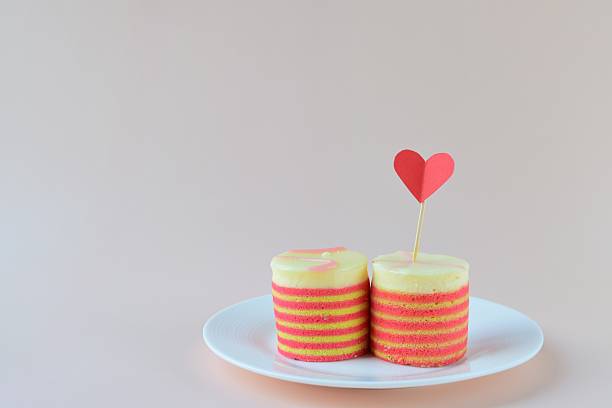 A plate with two delicious cakes and a paper heart on a pink background