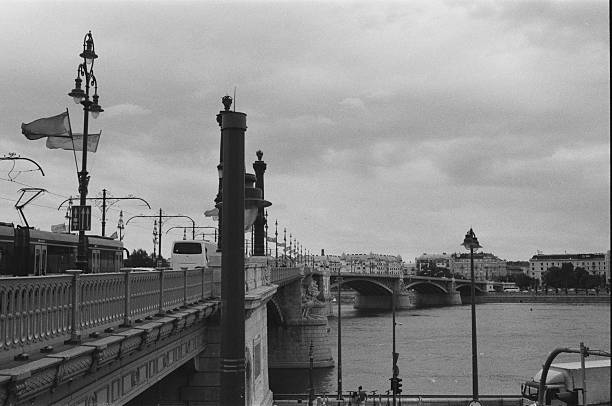 A city bridge over the Danube River in Budapest is photographed during daytime as part of a spring weekend trip, captured on black and white 35mm analog film with an analog camera.