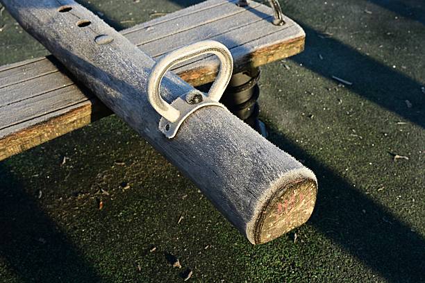 Empty spring-mounted seesaw dusted with frost on rubber safety surface, morning light.