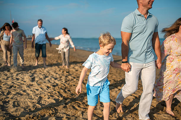 Families enjoying a day at the sandy beach, walking together under the bright sun. Adults and children sharing joyful moments by the ocean, creating lasting memories during their leisurely outing.