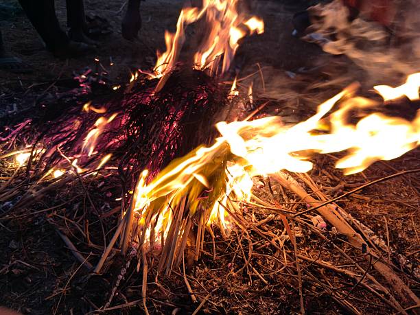 People warming their hands and feet over a glowing campfire. Bright orange flames flicker amidst charred wood and grey ash. This is a traditional way to keep the body warm during cold weather.