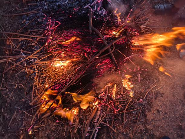 People warming their hands and feet over a glowing campfire. Bright orange flames flicker amidst charred wood and grey ash. This is a traditional way to keep the body warm during cold weather.