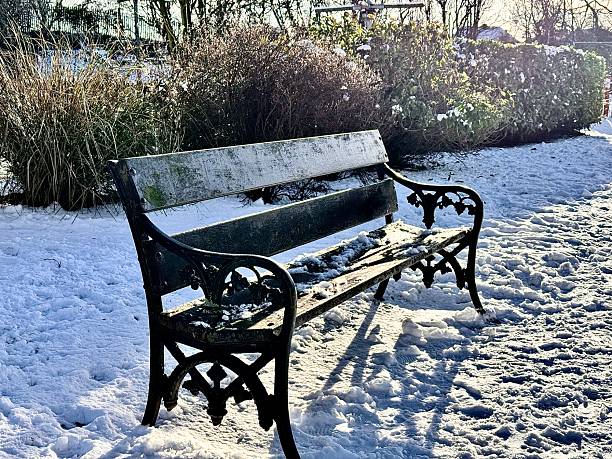 An empty public park bench on a cold winter day with snow on the ground at Blyth in Northumberland