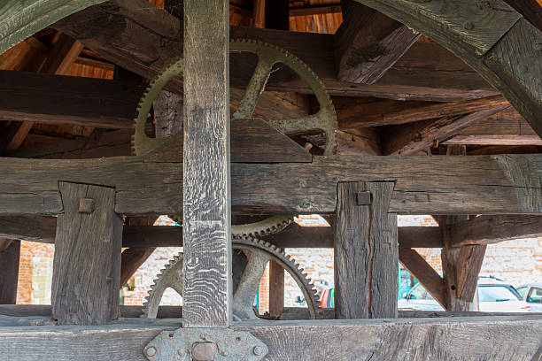 Close view of aged wooden beams and metal gears forming a traditional mechanical system inside an old mill structure. Strong textures, symmetry, and craftsmanship convey heritage engineering, manual technology, and historical construction methods.