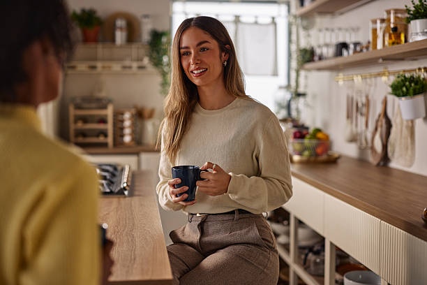 istock Woman in beige sweater seated at kitchen counter with mug, sharing a friendly conversation 2256437135