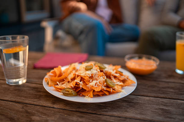 Friends enjoying a relaxed autumn gathering in a backyard patio setting. A rustic table features nachos with jalapeños, drinks, and a bowl of sauce, highlighting a casual social scene.
