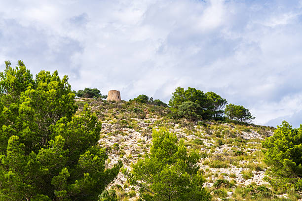 Historic stone watchtower Torre Nova des Cap Vermell overlooking Mediterranean coastline in Canyamel, Mallorca, Spain, surrounded by rocks and natural landscape.