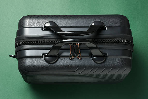Suitcase. High angle view a clean black suitcase on the green background. Closed suitcase with handles