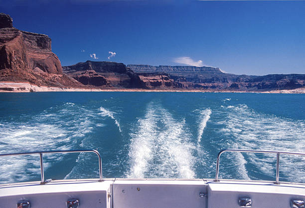 A serene view of Lake Powell with a marina filled with boats set against the dramatic sandstone cliffs and buttes of the surrounding desert landscape. The vivid blue sky and calm waters highlight the beauty of this iconic reservoir located on the Arizona–Utah border.