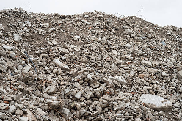 Pile of concrete rubble and broken construction debris with scattered metal pieces under cloudy sky, destruction and decay concept.