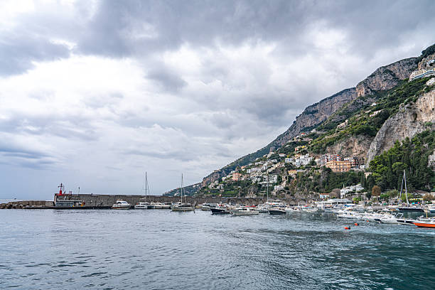 High-angle idyllic view of group of ships sailing the crystal blue sea by the old red roof houses on the green hills in Amalfi, South Italy