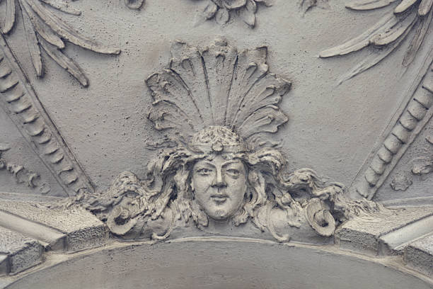 Close up of a stone carved female face ornament with a feather headdress on an old architectural facade