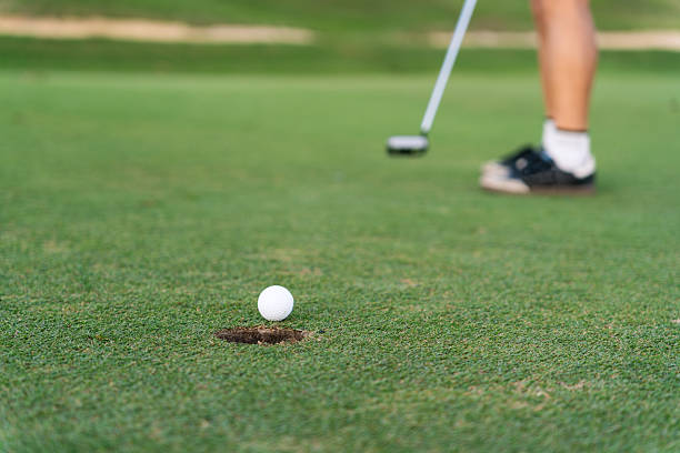 istock Unrecognizable golfer putting white ball toward hole on a pristine green under bright natural sunlight, close-up partial view of player 2256466315