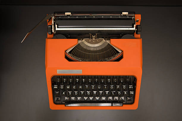 Old bright orange vintage manual typewriter with a qwertzu keyboard showing type bars and carriage, sitting on a dark grey surface, symbolizing creativity, nostalgia, and classic communication