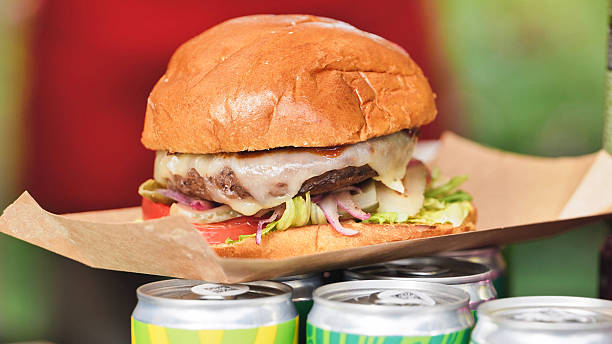Cheeseburger with melted cheese, lettuce, tomato, and pickles standing on beverage cans