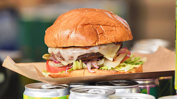 Cheeseburger on brown paper and cans, featuring melted cheese, beef patty, fresh lettuce, and red onion