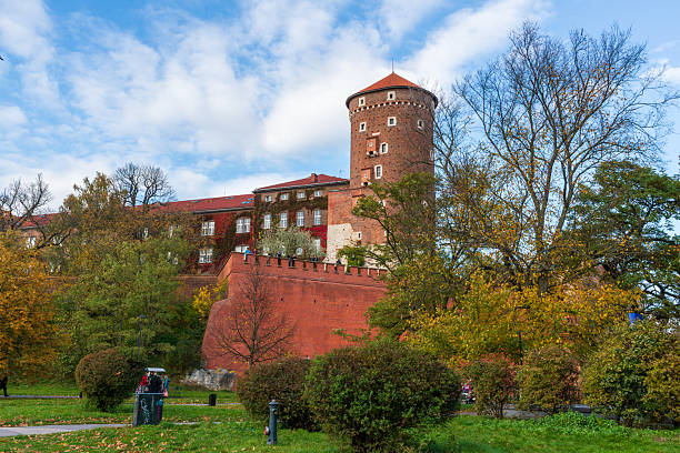 Krakow, Poland – October 25, 2025: The brick walls and towers of Wawel Castle rise above a park filled with autumn trees. Visitors walk along the paths, enjoying seasonal colors around one of Krakow most iconic landmarks.