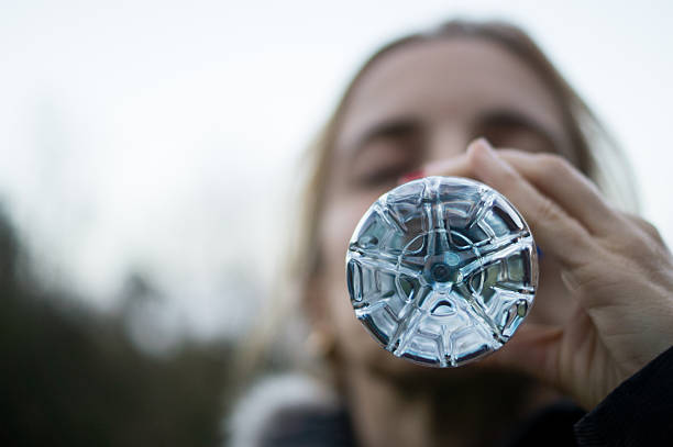 Profile view of a woman drinking from a plastic bottle with a large blurred area for copy space. Concept of microplastics, endocrine disruptors, and environmental health awareness.
