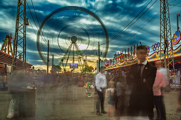 Slow shutter image captures the Ferris wheel and crowds at the April Fair in Seville, Spain. Dusk lighting illuminates the scene.