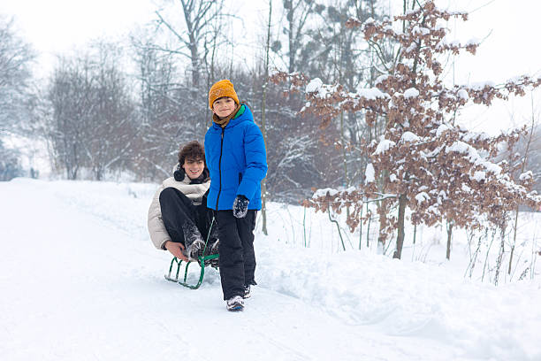 Two cheerful children in warm winter clothes sledding together on fresh deep snow, smiling and enjoying outdoor fun, sibling bonding and playful winter recreation