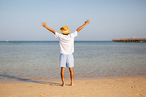 Man standing on sandy beach with arms raised, enjoying ocean view