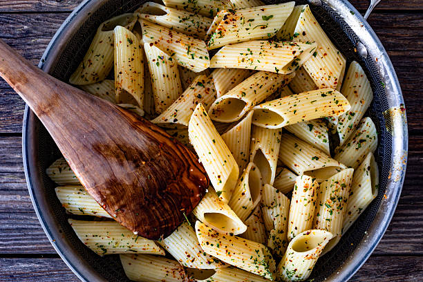 Penne pasta with herbs in frying pan on wodden background