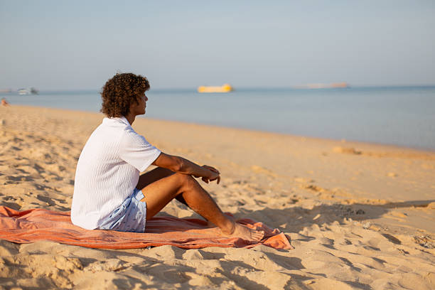 Young man sitting on towel at beach relaxing and looking at horizon