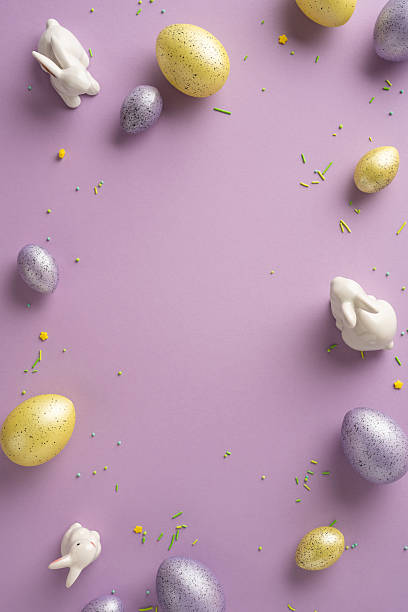 Pastel vertical eggs, white ceramic rabbits, and confetti on a lilac backdrop evoke Easter celebration, spring joy, and seasonal decor for greeting cards and stock photography