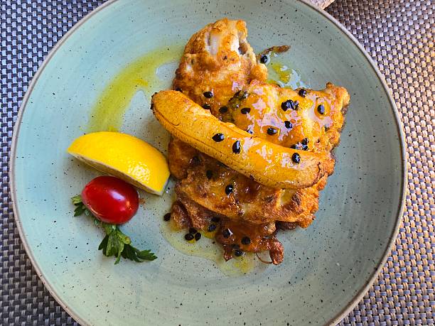 Overhead top-down view of Espada com Banana, a traditional Madeiran dish featuring fried black scabbardfish served with caramelised banana and passion fruit sauce, photographed in Madeira, Portugal. The composition highlights a vibrant colour contrast between golden-brown fried fish, bright yellow banana and lemon, glossy dark passion fruit seeds, and a muted green ceramic plate. Clean flat-lay presentation with natural textures, suitable for food, travel, gastronomy, and regional cuisine concepts.