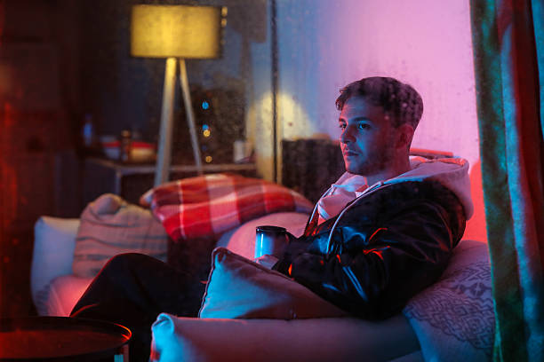 Young Man Drinking Hot Coffee at Home on Rainy Night with Neon Light Reflection on Window, Men's Lifestyle