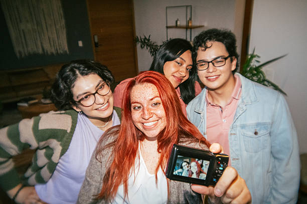 Group of friends take selfies with old digital camera. Shot with flash on camera and plastic lens to achieve a retro look.