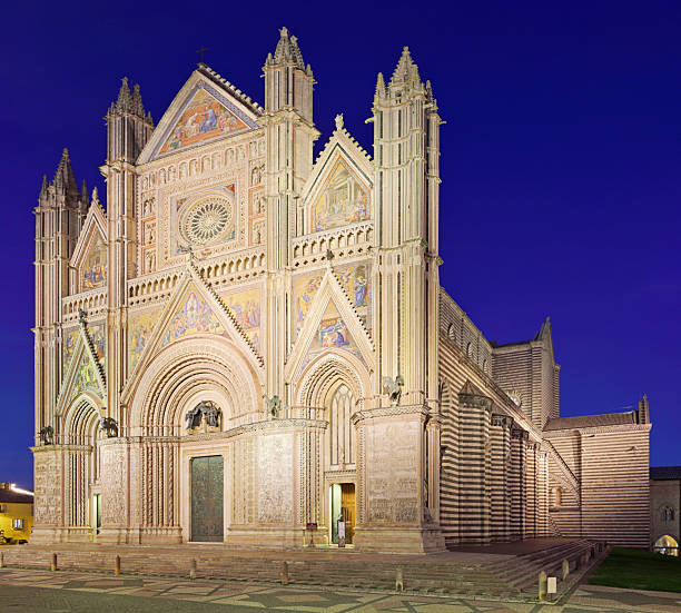 Orvieto Cathedral, also known as the Duomo di Orvieto, at night in the town of Orvieto, Umbria, Italy. Built between the 13th and 14th centuries, the Gothic cathedral is known for its richly decorated façade, mosaic details, and prominent rose window.