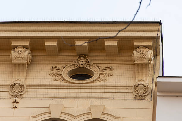 istock Decorative cornice of a historic building with stucco molding, oval window, and protective mesh against birds 2256496518