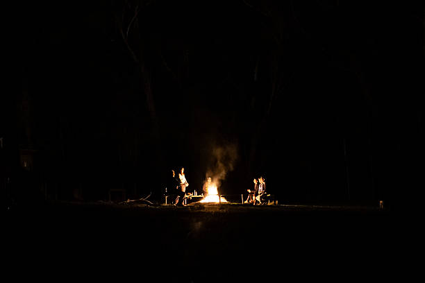People enjoying a quiet camping experience in a remote natural landscape, with mountains and forest framing a night sky filled with stars