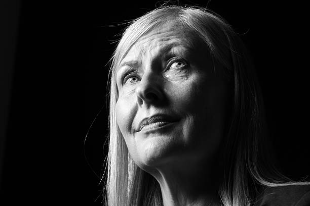Senior woman crying on dark background, low angle view. Black and white effect