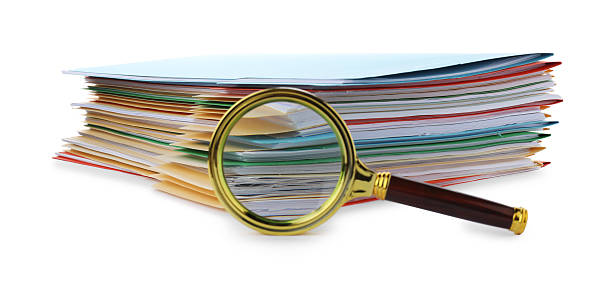 Stack of colorful folders with documents and magnifying glass isolated on white