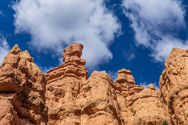 Stone hoodoo formations, Bryce Canyon National Park, Utah. Looking upwards from hiking trail. Cloudy blue sky in the background.