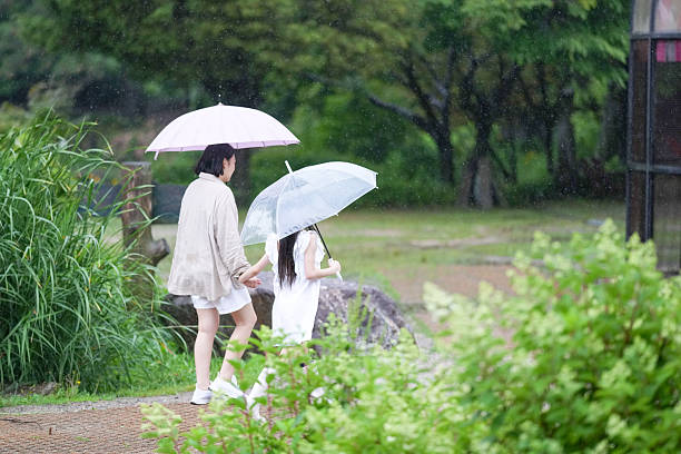 Two women walking in the rain with umbrellas. One of the umbrellas is pink