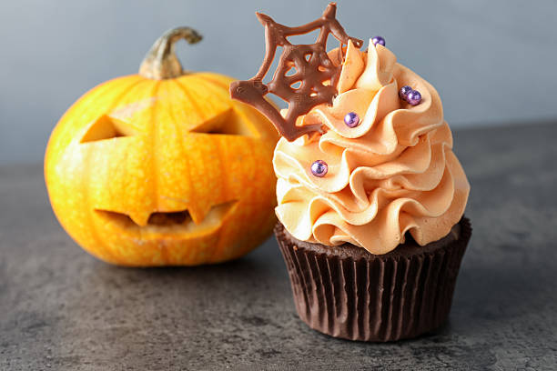 Delicious cupcake with chocolate web, sprinkles and pumpkin on grey textured table, closeup. Halloween celebration