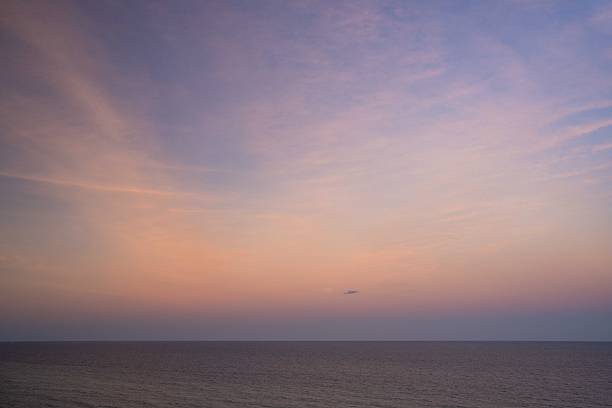 This serene coastal scene captures waves moving gently toward the shoreline as the sun sets, painting the sky in warm yellow tones and creating a calm, atmospheric beach moment