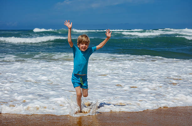 A young boy is happily splashing in the ocean waves while enjoying a sunny day at the beach, capturing the essence of fun and excitement during summer activities by the sea