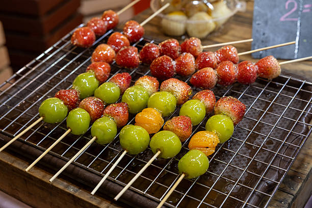 night market stall offers glossy, sugar-coated strawberry and grapes candy tanghulu, their vibrant red hue and crystalline glaze sparkling under warm lights.