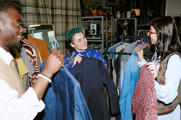 Group of multiethnic young adults browsing and selecting second hand clothing from racks in thrift store setting