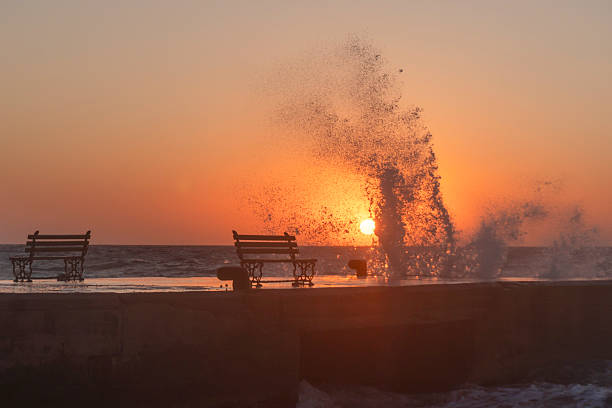 A wave hits the dock and the sun sets on the horizon