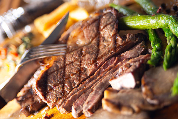 A mouthwatering close-up of a perfectly grilled beef steak sliced to reveal tender, juicy texture, with rich grill marks and natural meat fibers in sharp focus. Served with fresh asparagus and rustic sides on a wooden board, this image conveys premium steakhouse quality and indulgent dining.Perfect for restaurant menus, gourmet food branding, culinary editorials, advertising campaigns, food blogs, and high-end stock photography. Engineered to trigger appetite, trust, and purchase intent.