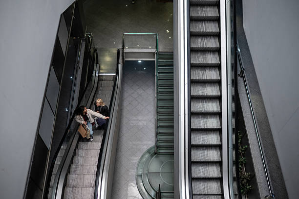 Two women having a conversation while riding an escalator in a modern urban shopping mall, seen from an aerial view
